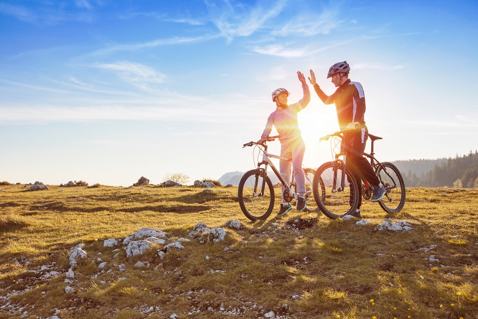 happy couple goes on a mountain asphalt road in the woods on bikes with helmets giving each other a high five.